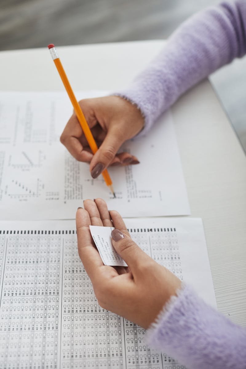 Close-up of a student writing answers during an exam using a cheat sheet in hand.